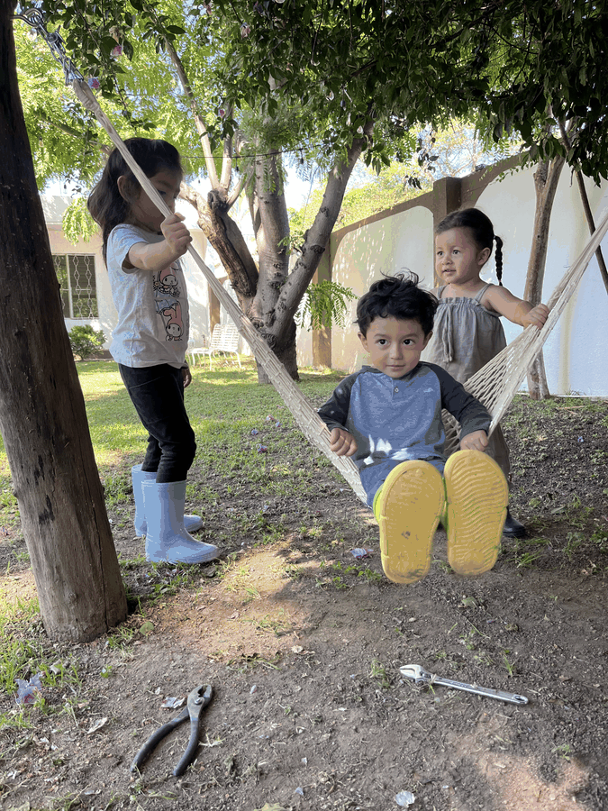 Niños jugando en un columpio bajo un árbol
